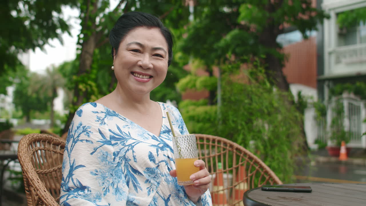 Positive Aged Woman Drinking Orange Juice in Outdoor Cafe