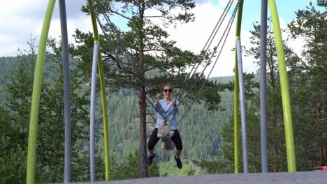 childish adult woman having fun riding chain and rope swing inside bjorneparken theme park in norway