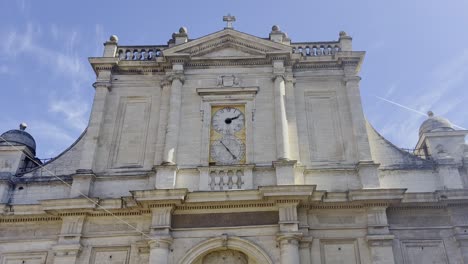 Front-of-a-church-building-in-a-small-town-in-France-made-of-sandstone-with-a-large-clock,-some-columns-and-decorations