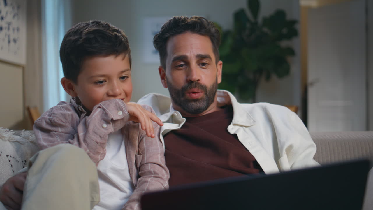Family engrossed funny movie relaxing at home closeup. Daddy son with laptop