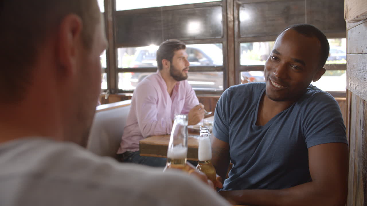 Two male friends talking at a make a toast with beer bottles