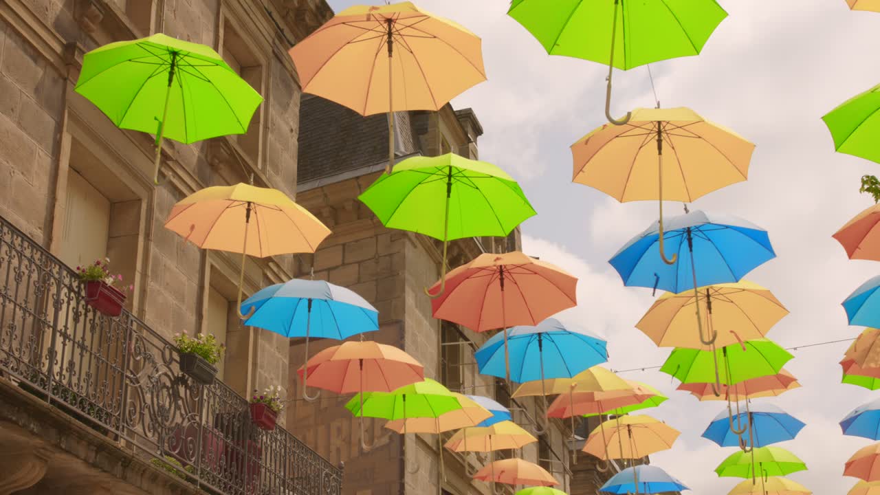 Orange, green and blue umbrellas suspended above a cobbled street in Brive-la-Gaillarde during summer season