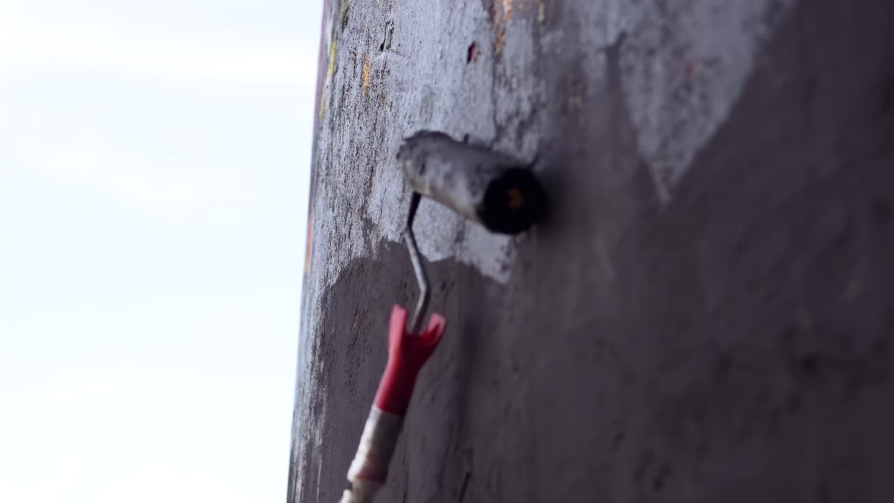 Close up of a roller brush painting with black dye on a construction site wall