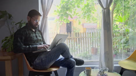 man working on laptop at home office by window