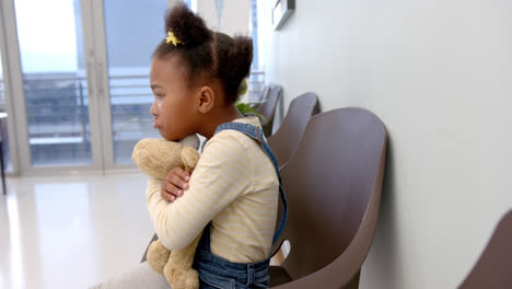 sad african american girl sitting in hospital waiting room and holding mascot, slow motion