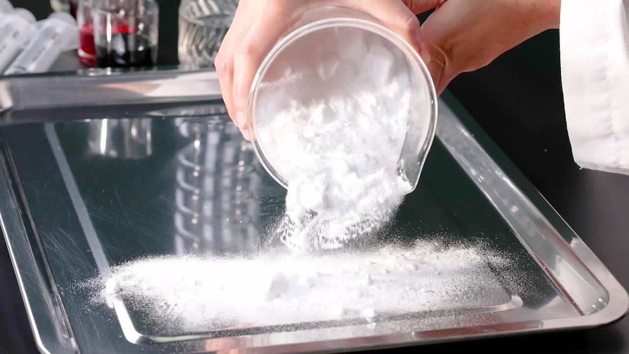 una persona vierte bicarbonato de sodio en una bandeja de metal, mostrando un simple experimento científico con iluminación clara y brillante