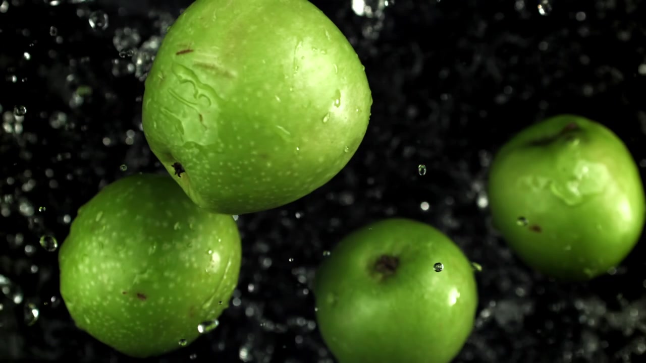 Mele verdi fresche che schizzano con goccioline d'acqua su sfondo nero