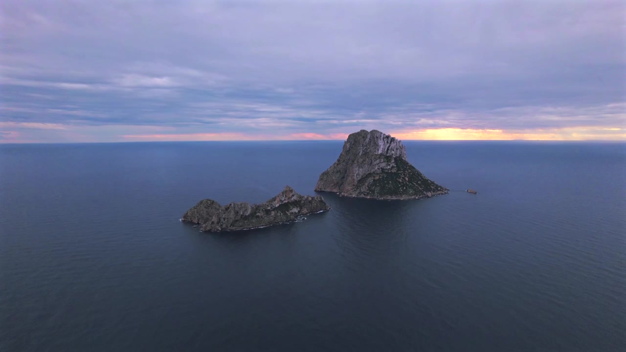 Ripresa aerea in 4K con drone di Es Vedrà al tramonto, Ibiza, Spagna. L'iconica isola rocciosa emerge dal Mar Mediterraneo mentre una calda luce dorata illumina la costa e le acque circostanti
