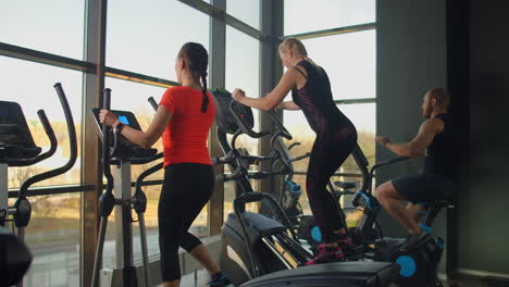 young fit woman using an elliptic trainer in a fitness center. a group of young women train on sports training equipment in a fitness gym. steady cam shot.