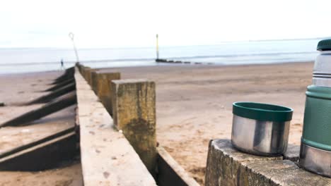 Drinking-hot,-steaming-tea-from-a-flask,-on-a-beach