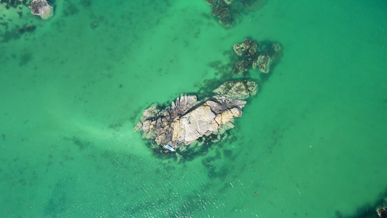 un hombre de pie en una pequeña isla rocosa con un paddleboard rodeado de agua de mar turquesa en un lago en las tierras altas escocesas