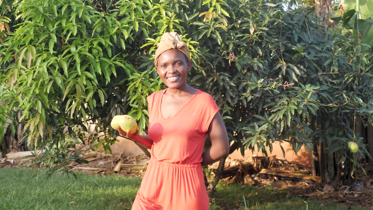 Donna africana che cammina portando manghi appena raccolti nell'Africa rurale mentre sorride