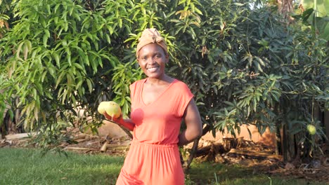Afrikanische-Frau,-Die-Geht,-Während-Sie-Frisch-Gepflückte-Mangos-Im-Ländlichen-Afrika-Trägt,-Während-Sie-Lächelt