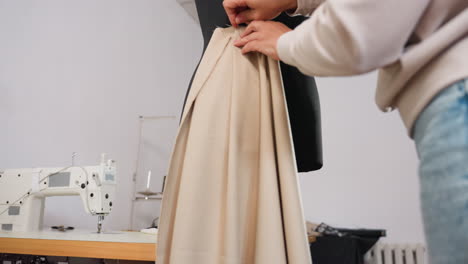 fashion designer fitting apparel on waist line of black mannequin beside electric sewing machine, carefully adjusting fabric, focusing on skillful draping, ensuring polished silhouette