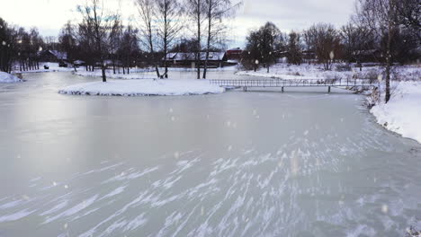 frozen lake water in city park during majestic snowfall in aerial low altitude flying shot