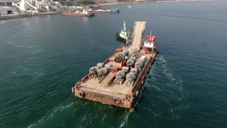 Barge-loaded-with-Concrete-mixer-trucks-pulled-to-port-by-a-Tugboat-in-Hong-Kong-bay,-Aerial-view