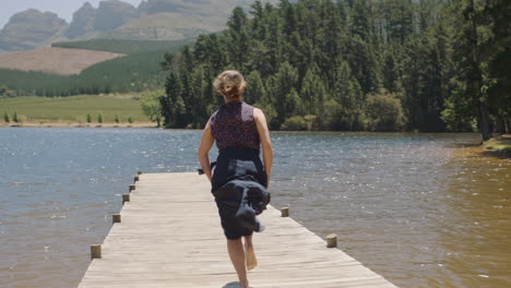 young woman running jumping off jetty in lake splashing in water enjoying summer freedom