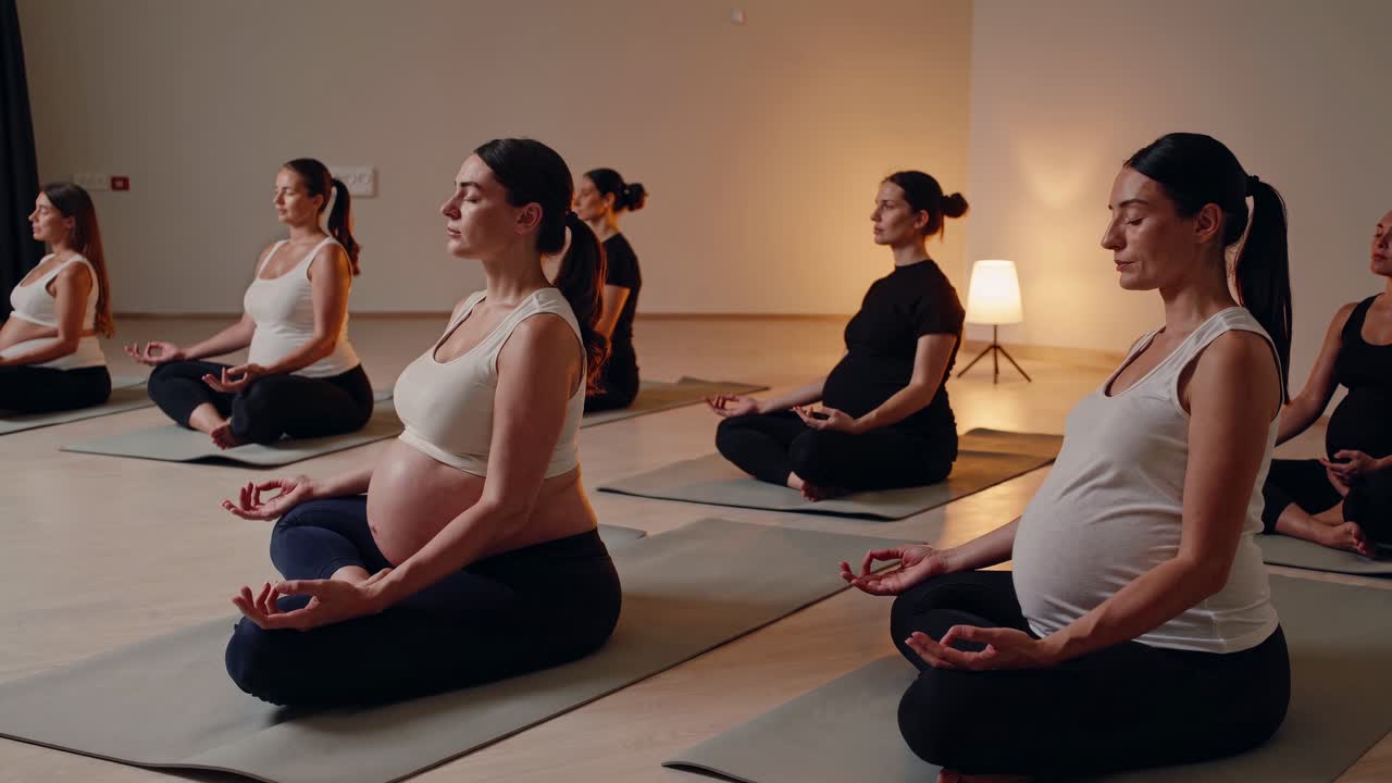 Pregnant women in a yoga class, meditating on mats. Side angle captures calm ambiance. Ideal