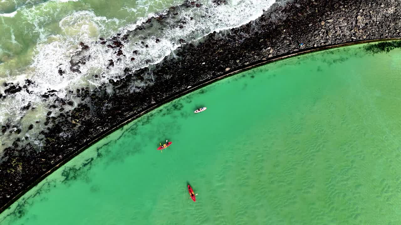 Drone clip of canoeists rowing in a tidal pool with the ocean waves crashing against the rocks in the background