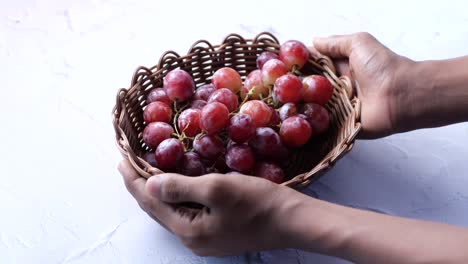 primer plano de manos sosteniendo una canasta de uvas rojas
