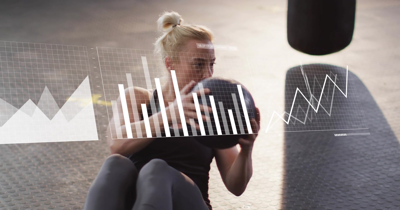 Woman twisting med ball on mat facing heavy bag animating HUD building fitness graphs, world map