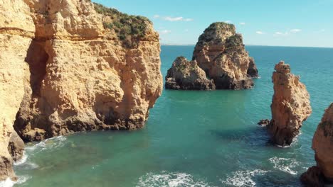 sea eroded rocky sprouts scattered along algarve shore, in lagos, portugal - aerial low angle fly-over shot