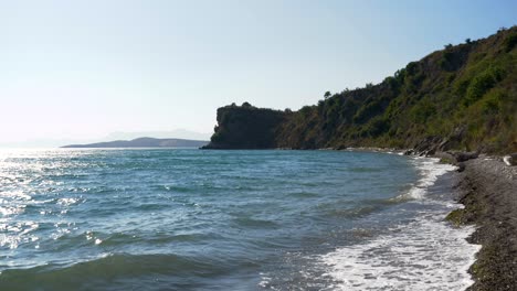 Beach-in-Greece,-tall-green-cliff-above-the-waves-of-the-Ionian-Sea