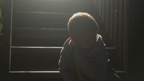 preschooler child silhouette on stairs in evening. cute boy sits alone on steps at cottage house. kid rests on staircase of eco hotel at backlight