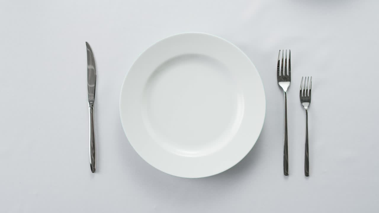 Professional table setting with white gloves. Plates, fork, knife, and glass arranged on a white table.
