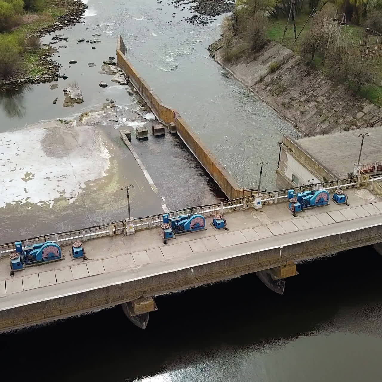 A huge construction with a bridge stands on the river outside the city for water purification on the background of wonderful landscape of green trees and with buildings. Close-up. Aerial view.