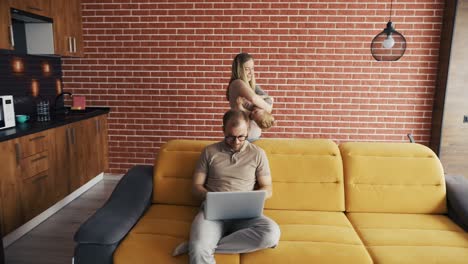 Mother-plays-with-her-son-at-home-while-their-father-busy-with-laptop-on-the-sofa