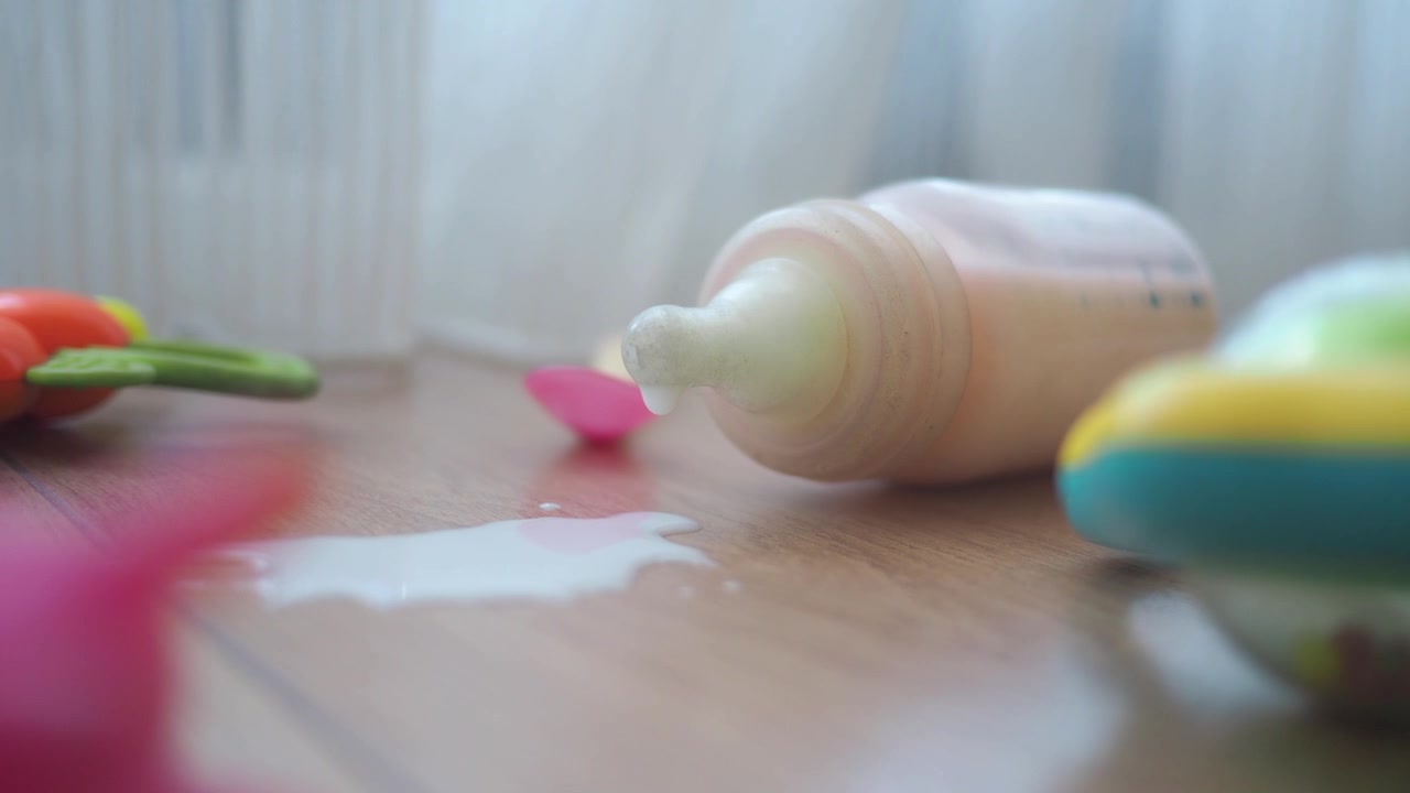 Spilled Baby Bottle with Milk on Wooden Floor