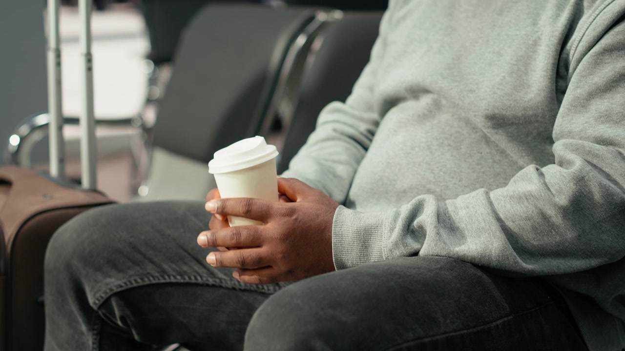 Primo piano di un passeggero con tazza di caffè da asporto in stazione degli autobus