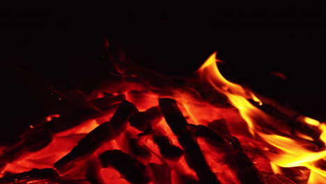 a pile of burnt wood with flames on one side. campfire turned into smoldering embers. close up. black backdrop.