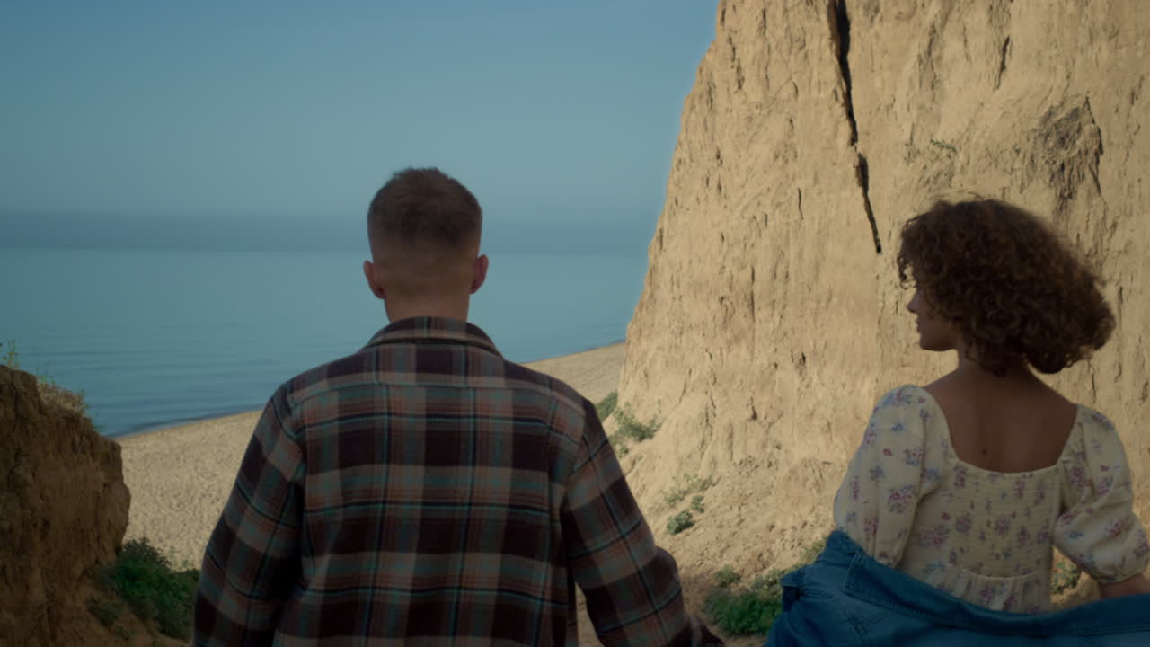 una pareja bajando por la costa a una playa de arena. una mujer feliz mirando con adoración al hombre.