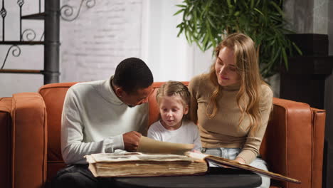 black man shows photo to little girl with wife on sofa