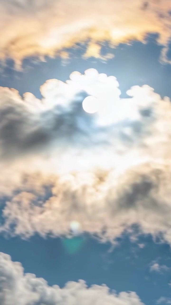 Video verticale: Nuvole che si spostano rivelano il sole su un cielo azzurro, mosse dal vento, producendo abbagliamento e bagliori.