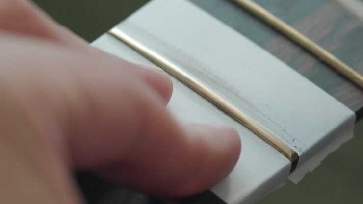 Liutaio che lucida i tasti di una chitarra acustica usando bastoncini lucidanti con carta vetrata a micro-rete.