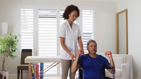 mixed race female physiotherapist helping senior man exercise using dumbbells