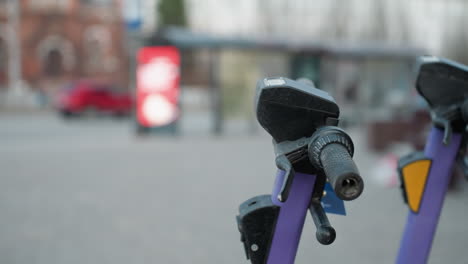 close view of purple electric scooters parked in a busy city area, the background includes blurred cityscape with moving cars and people