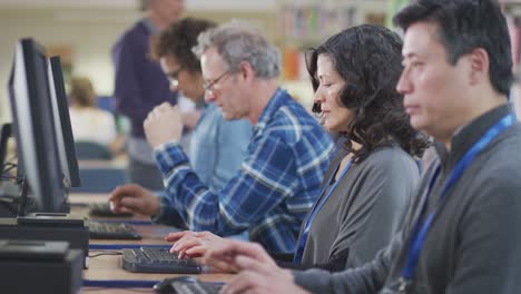 Group Of Mature Adult Students In Class Working At Computers In College Library