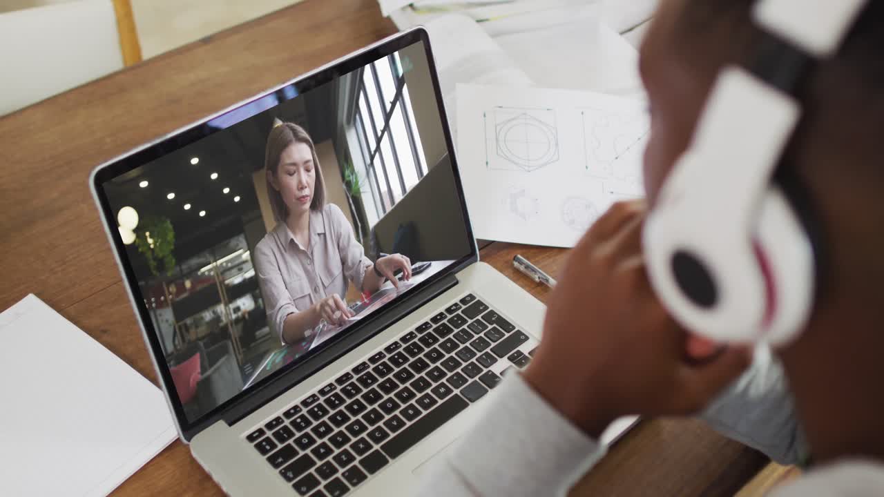 African american male college student holding notes while having a video call on laptop at home