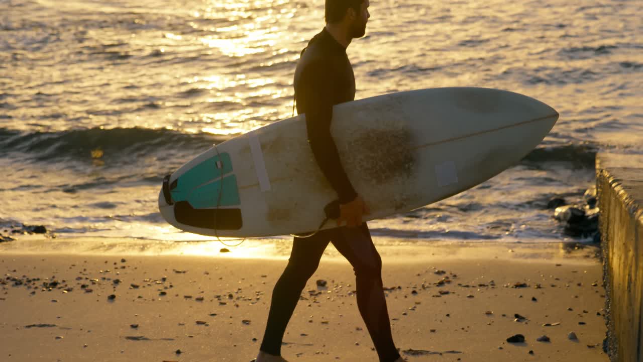vista lateral de un surfista caucásico adulto caminando con una tabla de surf en la playa 4k