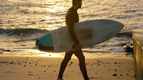 side view of mid-adult caucasian male surfer walking with surfboard at the beach 4k