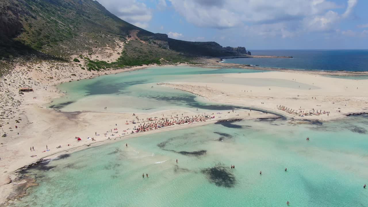 Balos Beach blue saltwater lagoon in Crete Greece with bathing tourists, Aerial dolly out shot