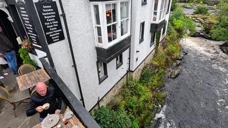 man enjoys coffee beside scenic welsh stream