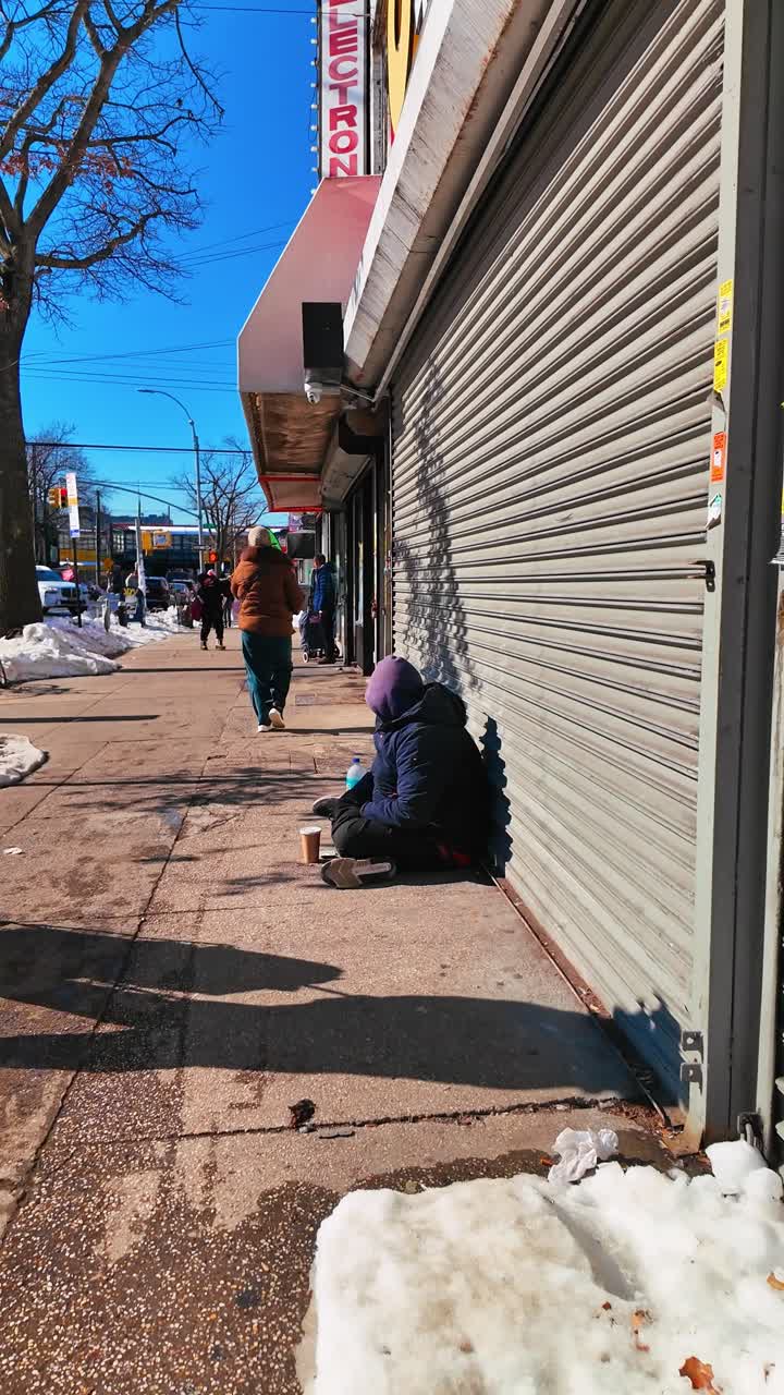 New York, VS, 25 december 2025: Persoon zittend op de stoep bij gesloten metalen winkelrolluiken. Lage camerahoek van een persoon die rust tegen een gesloten winkelpui in een besneeuwde New Yorkse straat.