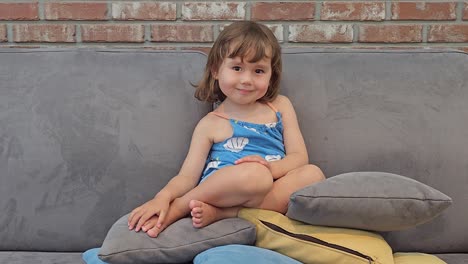 Cheerful-3-Years-Old-Girl-Sitting-On-A-Couch-on-Top-Of-Throw-Pillows-At-Home