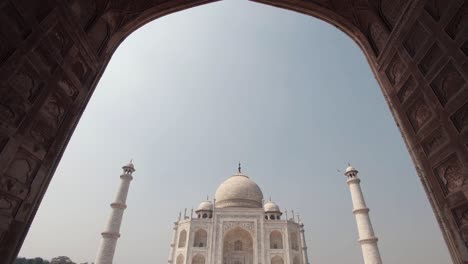 reveal of divine taj mahal glorious against blue sky from mosque entrance main arch - wide tilt down reveal