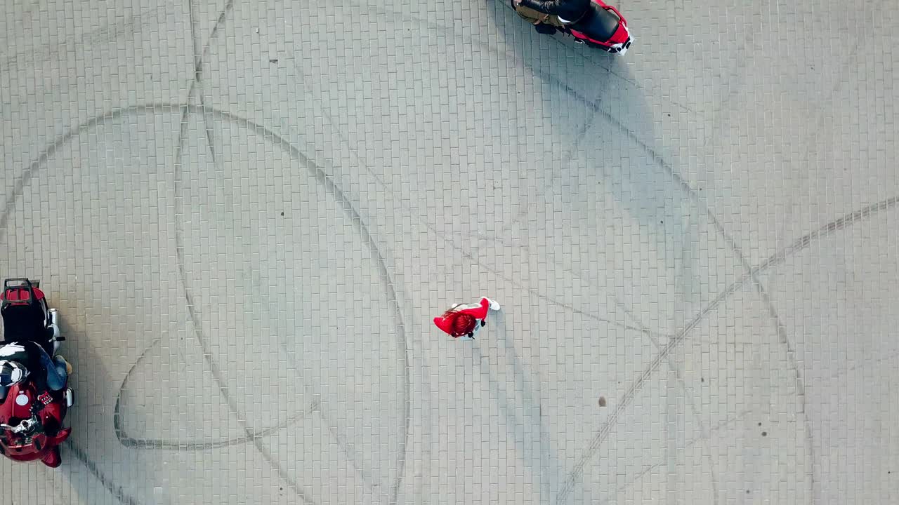Red-haired woman standing in the centre of two professional motorcyclists riding around her. Top view of a beautiful young female and motorbikers on the road.